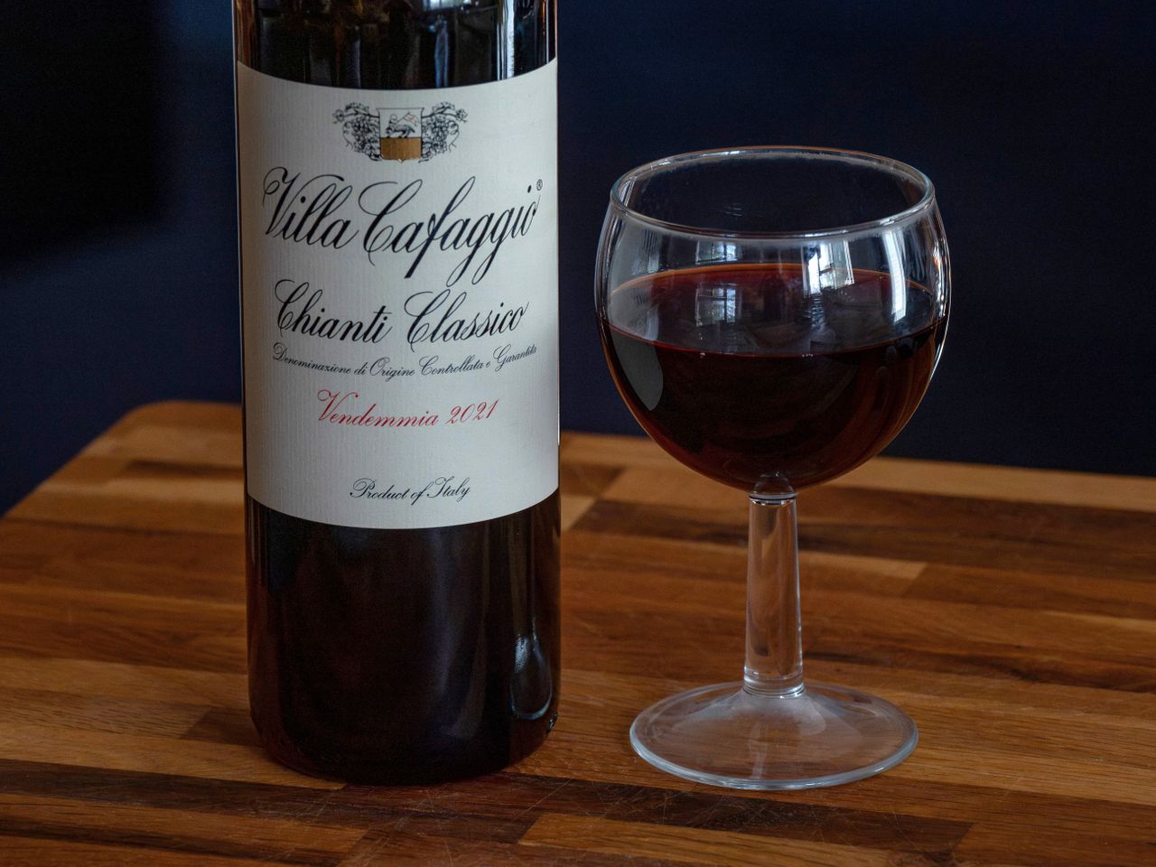 A bottle of Villa Cafaggio Chianti Classico 2021 and a glass of red wine on a wooden surface.